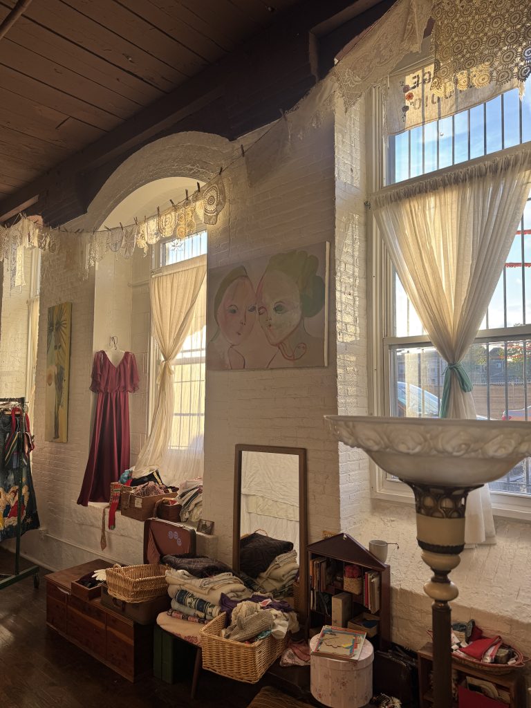late afternoon light streaming in large windows a 1970s gown in hanging in the arch of one window, baskets of accessories are on a bench below.